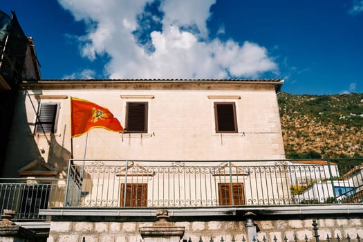 Flag of Montenegro flutters on a flagpole on the terrace of an ancient stone house at the foot of the mountains. High quality photo