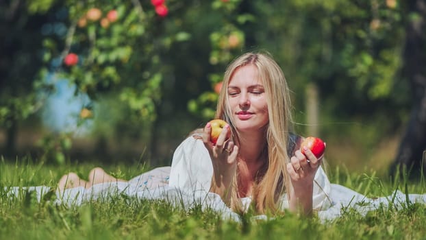 A young woman is lying on the grass in the garden eating an apple