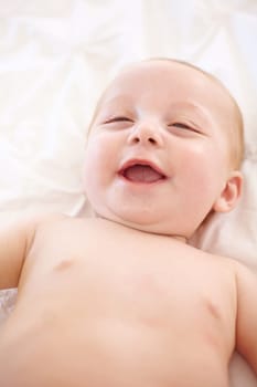 Happy baby on bed, funny and top view of young child in development, innocent or relax at home. Kid smile above, infant laughing in nursery and rest in bedroom, healthy body or skin, cute or adorable.