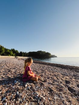 Little girl sitting on a pebble beach by the sea. High quality photo