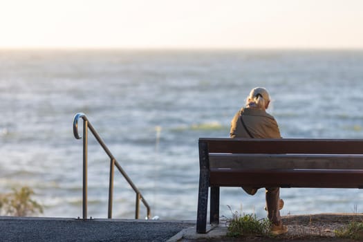 Back view of senior woman sitting on a bench at the beach a sunny day