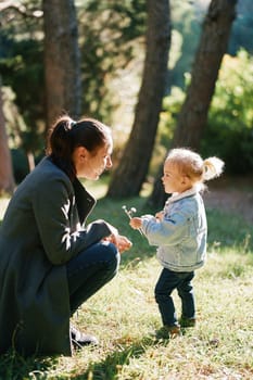 Little girl with wildflowers stands near her mom squatting in the forest. High quality photo