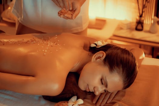 Woman customer having exfoliation treatment in luxury spa salon with warmth candle light ambient. Salt scrub beauty treatment in Health spa body scrub. Quiescent