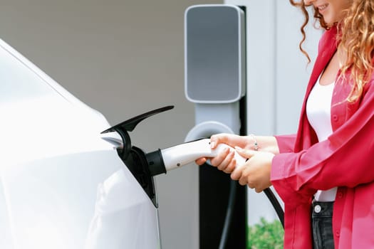 Modern eco-friendly woman recharging electric vehicle from home EV charging station. EV car technology utilized for home resident to future environmental sustainability. Synchronos