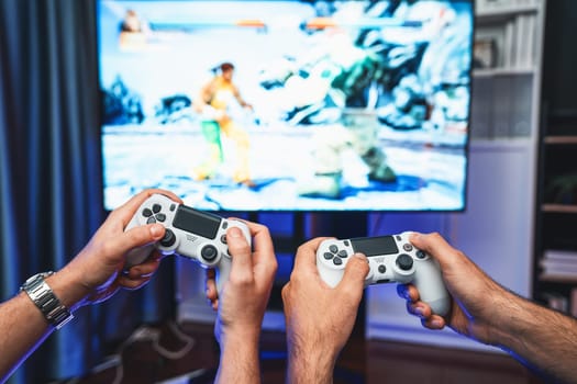 Friend gamers playing video game of battle martial arts fighter on TV using joysticks position of backside background. Comfy living neon light at home place with cheerful fighting winner. Sellable.