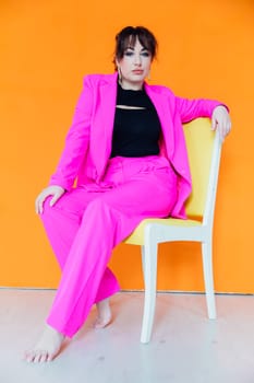 Woman in bright suit posing on a chair on an orange background