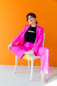 Woman in bright suit posing on a chair on an orange background