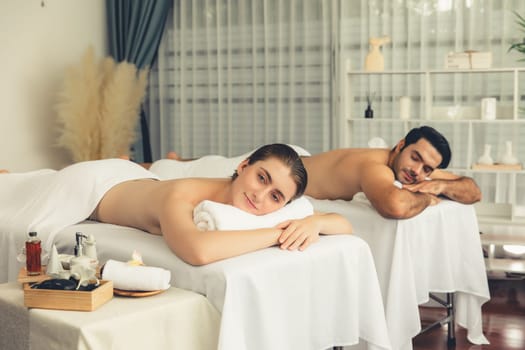 Caucasian couple customer enjoying relaxing anti-stress spa massage and pampering with beauty skin recreation leisure in day light ambient salon spa at luxury resort or hotel. Quiescent