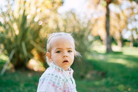 Little girl stands in a green garden with her mouth open. High quality photo