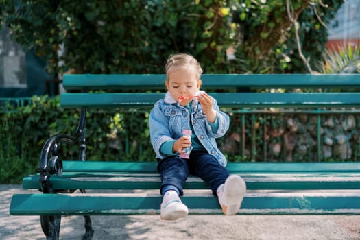 Little girl sits on a bench and blows soap bubbles. High quality photo