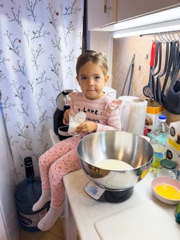 Little girl with a glass of milk in her hands sits on a table near the scales. High quality photo