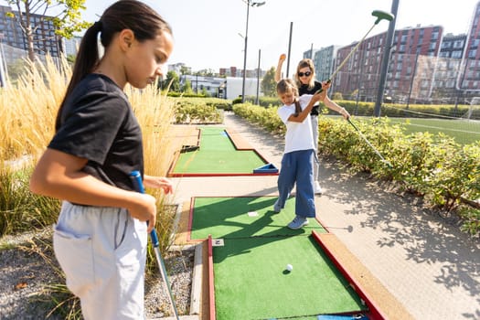 Cute school girl playing mini golf with family. Happy toddler child having fun with outdoor activity. Summer sport for children and adults, outdoors. Family vacations or resort. High quality photo