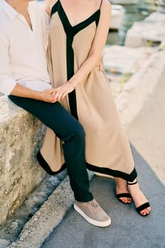 Woman sits on man lap, holding his hand on the stone pier. Cropped. Faceless. High quality photo