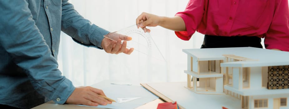 Young smart architect sends architectural equipment to project manager for measuring a house model and architectural equipment placed on meeting table. Creative design and teamwork. Variegated.