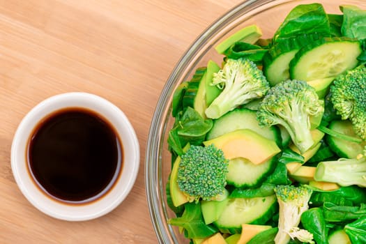 Fresh Green Salad of Avocado, Broccoli, Spinach and Cucumber for Detox with Soy Sauce on Wooden Cutting Board. Vegan Salad. Vegetarian Culture. Raw Food. Healthy Eating and Vegetable Diet