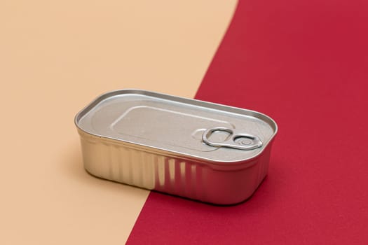 Unopened Tin Can with Blank Edge on Split Red and Beige Background. Canned Food. Aluminum Can for Safe and Long Term Storage of Food. Steel Sealed Food Storage Container