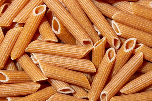 Uncooked Whole Grain Penne Rigate Pasta: A Culinary Canvas of Whole Wheat Macaroni, Creating a Lively and Textured Background for Gourmet Cooking. Whole Grain Dry Pasta. Whole Wheat Raw Macaroni