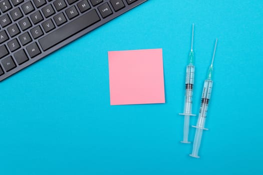 Vaccination, Immunology or Revaccination Concept - Two Medical Disposable Syringe Lying on Blue Table in Doctor's Office in a Hospital or Clinic. Blank Pink Sticky Note - Mock Up with Copy Space