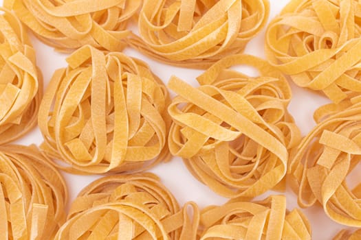 Scattered Classic Italian Raw Egg Fettuccine on White Table. Dry Twisted Uncooked Pasta. Italian Culture and Cuisine. Raw Golden Macaroni Pattern
