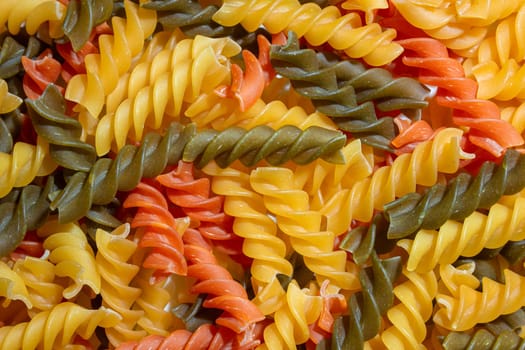 Uncooked Vibrant Colored Fusilli Pasta: A Mesmerizing Culinary Canvas of Multicolored Spirals, Creating a Lively and Textured Background for Gourmet Cooking. Colored Dry Pasta. Raw Macaroni