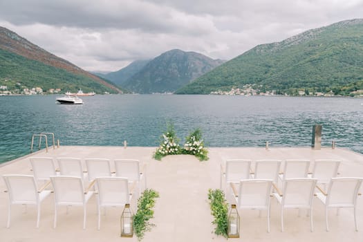 Rows of chairs stand on the pier in front of a floor wedding arch. High quality photo