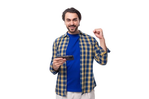 a young caucasian brutal man with an unshaven face dressed in a blue plaid shirt is watching a video on the phone.