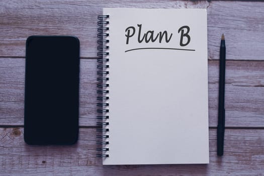 Plan B written on notepad with smartphone and pen on wooden desk. Backup plan concept.