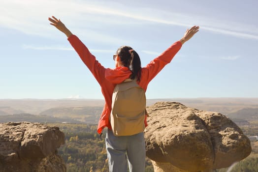 Active young woman with backpack hiking in the mountains with her arms raised up.