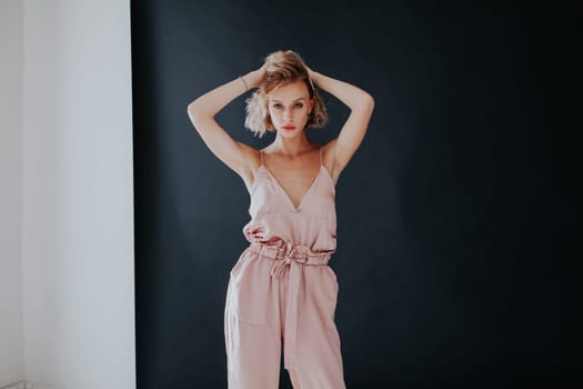 portrait of a beautiful fashionable woman in a pink jumpsuit against a black background