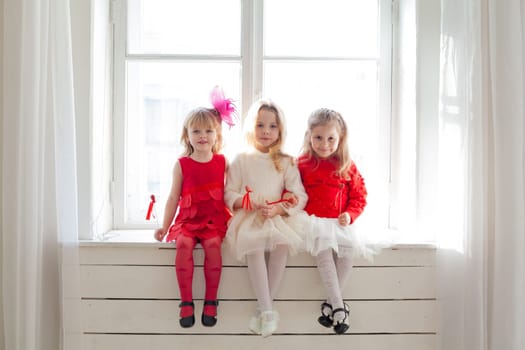 three girls in red and white clothes on holiday sit by the window