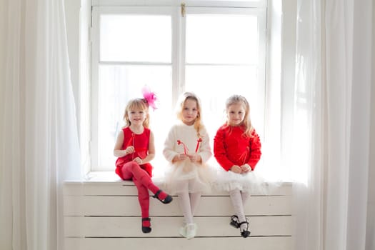 three girls in red and white clothes on holiday sit by the window