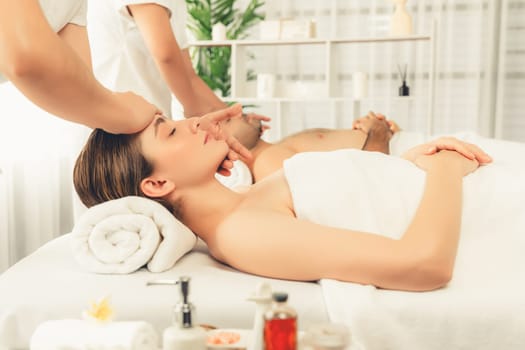 Caucasian couple enjoying relaxing anti-stress head massage and pampering facial beauty skin recreation leisure in dayspa modern light ambient at luxury resort or hotel spa salon. Quiescent