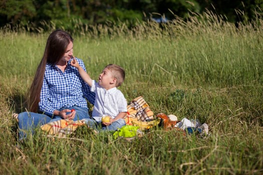 woman with her son on a picnic in a field near the forest