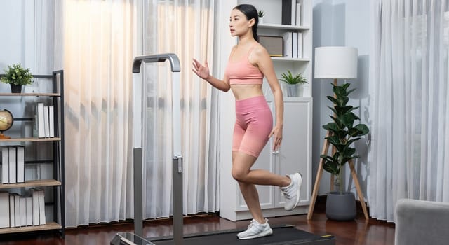 Energetic and strong athletic asian woman running running machine at home. Pursuit of fit physique and commitment to healthy lifestyle with home workout and training. Vigorous