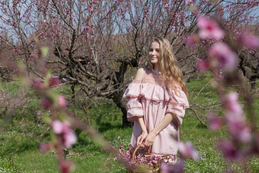 happy blonde woman in pink dress collects flowers in the flowering garden in spring
