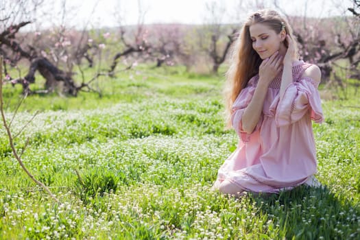 happy blonde woman in pink dress collects flowers in the flowering garden in spring