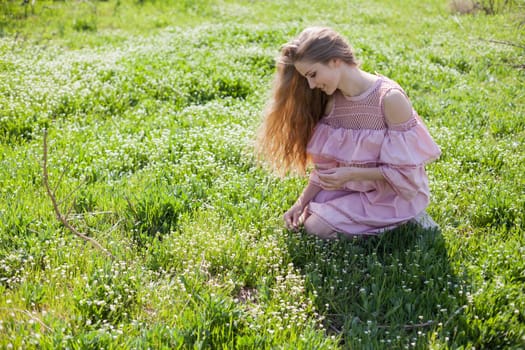 happy blonde woman in pink dress collects flowers in the flowering garden in spring