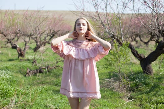 Beautiful happy blonde woman in pink dress walks through the flowering garden in spring