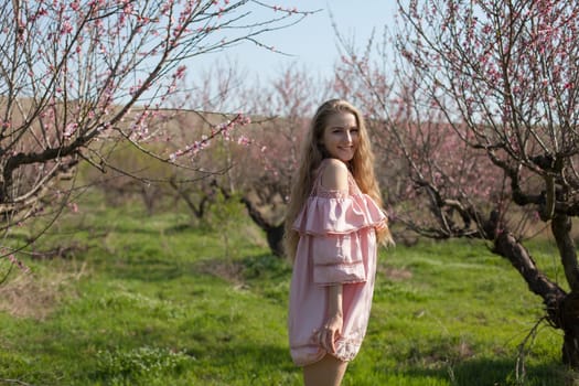 Beautiful happy blonde woman in pink dress walks through the flowering garden in spring