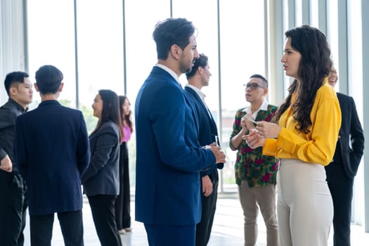 Businessman discussing with female leader about financial project intentionally while standing rounded with business people exchanging financial experience. Side view. Office hallway. Intellectual.