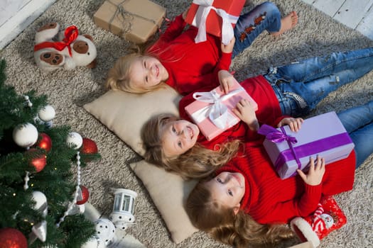 Three little girl girlfriends open gifts at the Christmas tree new year winter