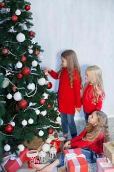 Three little girl girlfriends open gifts at the Christmas tree new year winter