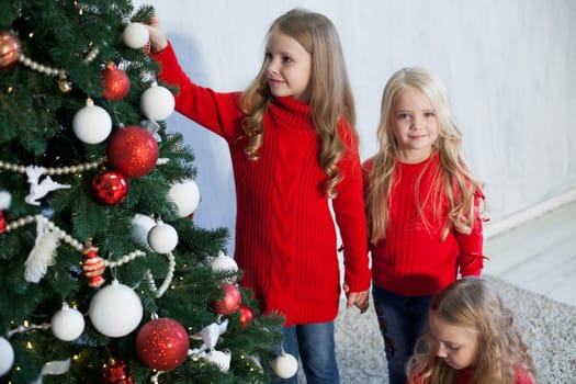 Three little girl girlfriends open gifts at the Christmas tree new year winter