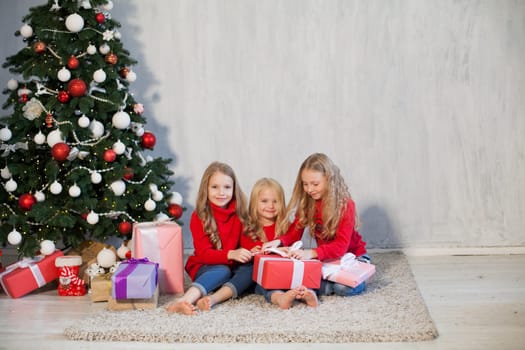 Three little girl girlfriends open gifts at the Christmas tree new year winter