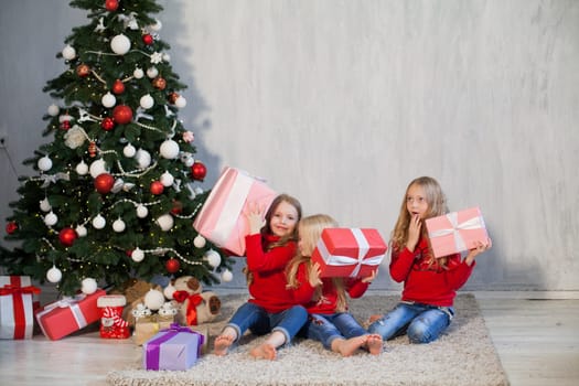 Three little girl girlfriends open gifts at the Christmas tree new year winter
