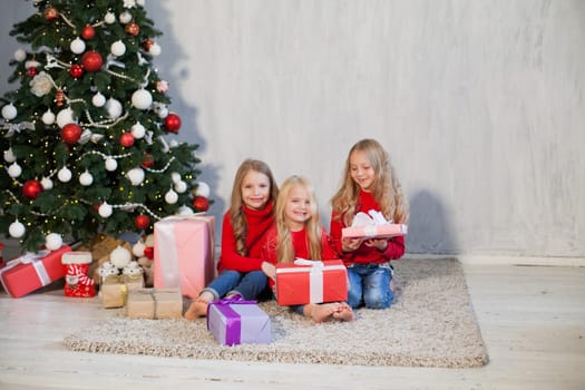 Three little girl girlfriends open gifts at the Christmas tree new year winter