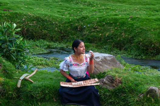 indigenous girl sitting next to a river tasting a large guaba, the girl wears a traditional dress from her culture. High quality photo
