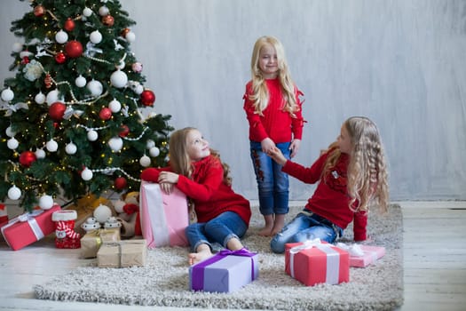 Three little girl girlfriends open gifts at the Christmas tree new year winter