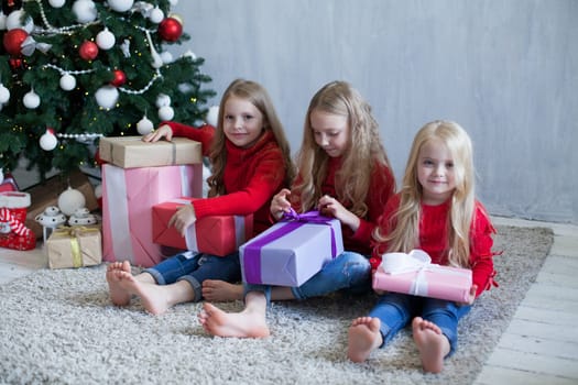 Three little girl girlfriends open gifts at the Christmas tree new year winter