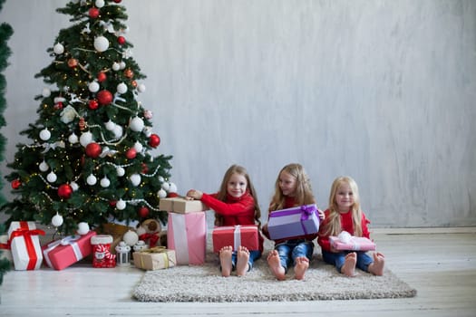 Three little girl girlfriends open gifts at the Christmas tree new year winter